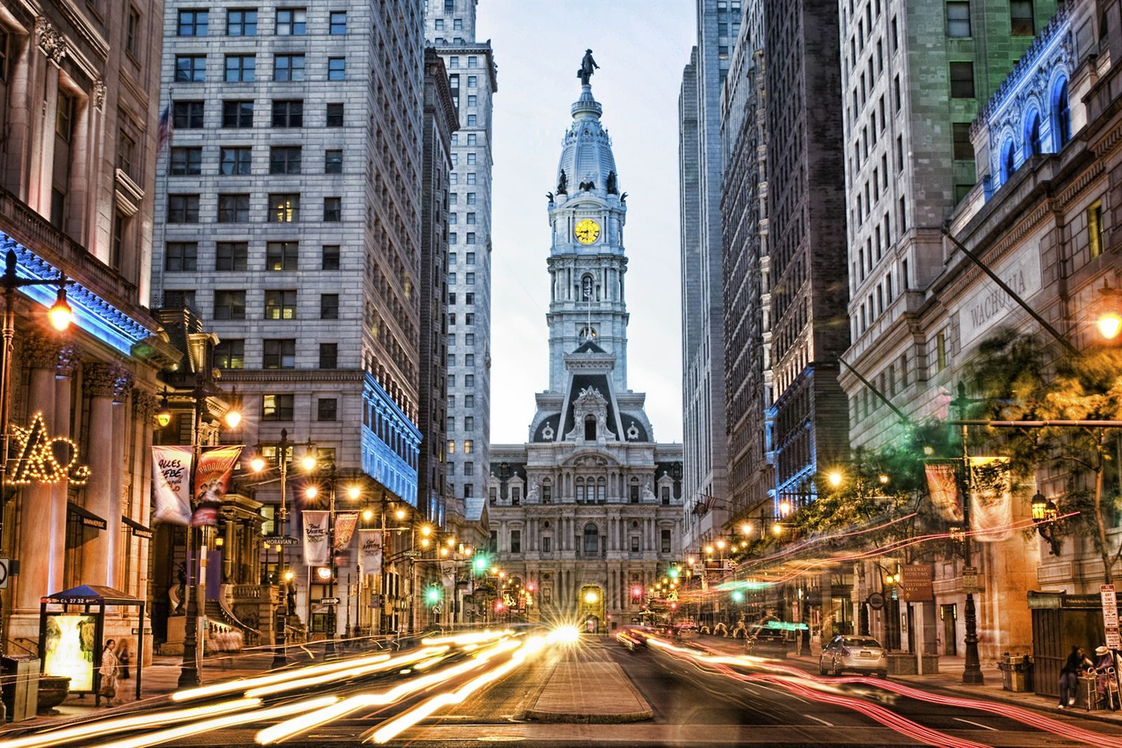 Broad Street at night leading to Philadelphia City Hall and its William Penn statue, lined with lit restaurants and theaters