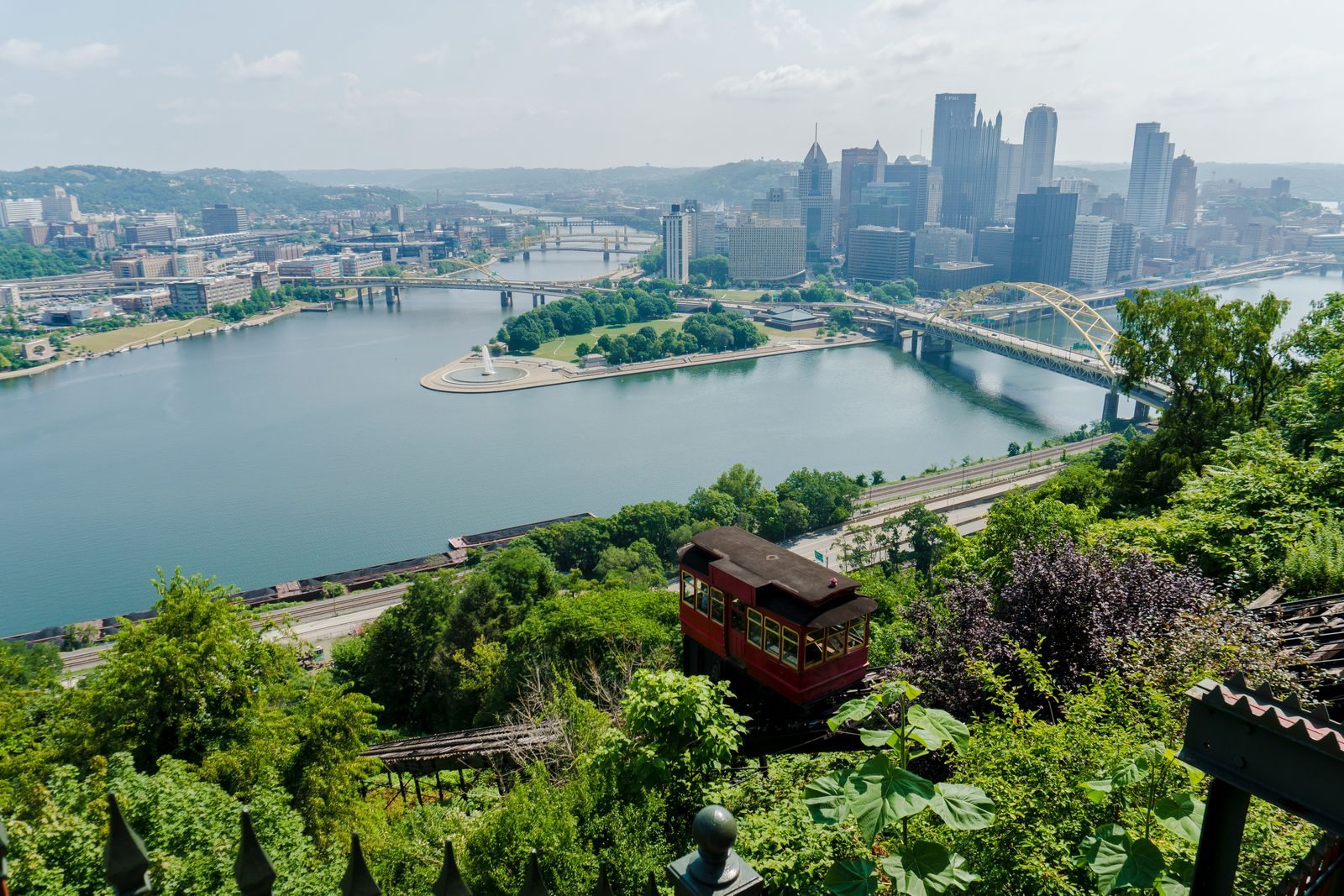 A red incline car climbing Mount Washington above the rivers and downtown Pittsburgh